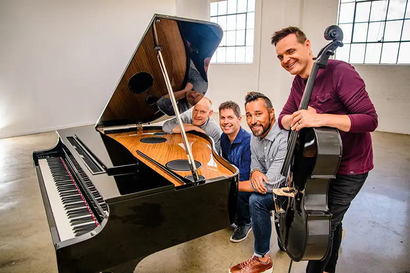 The Piano Guys gathered around an open Yamaha grand piano, one holding a cello